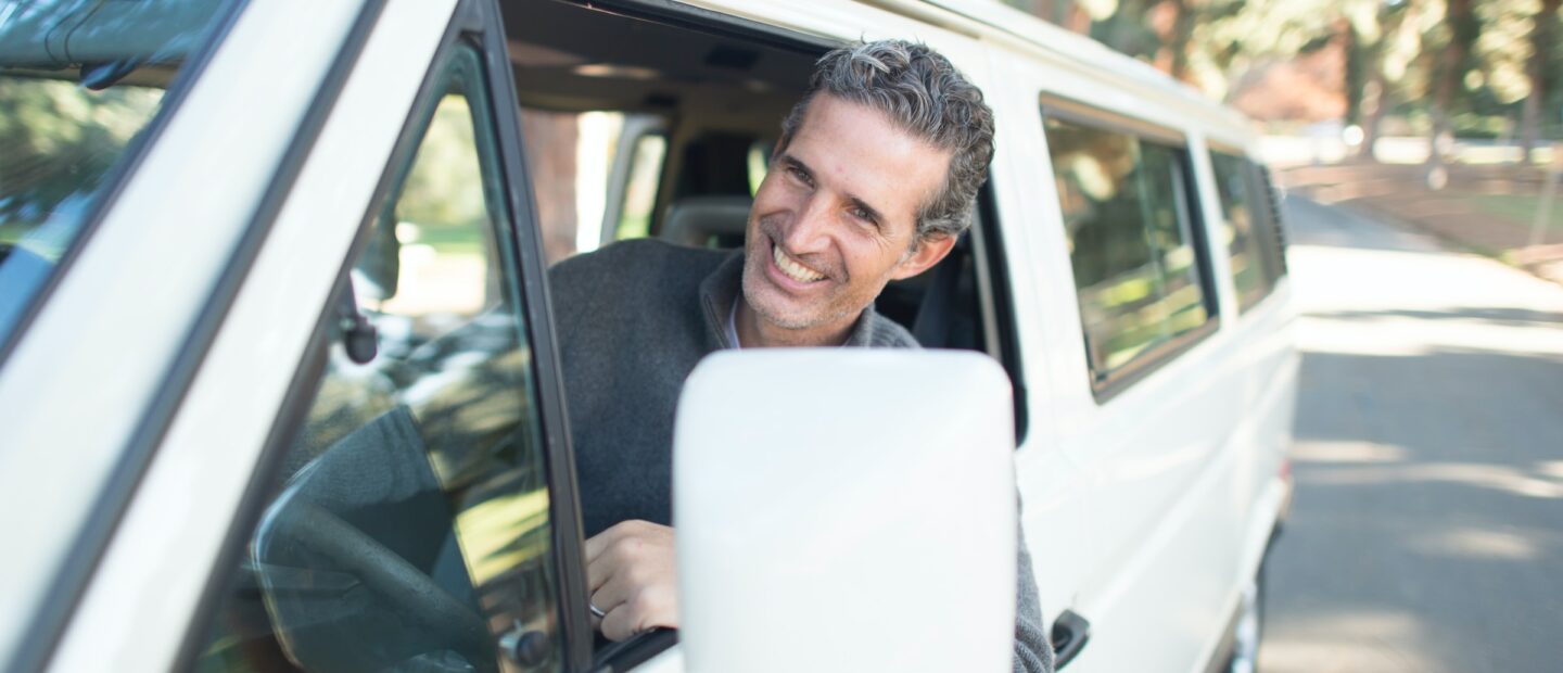 Smiling man with arm out the window driving a white van
